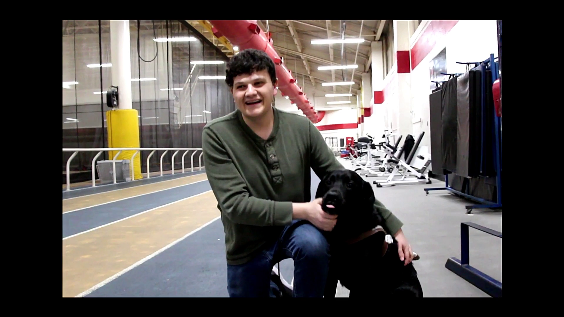 man with curly hair kneels beside a guide dog